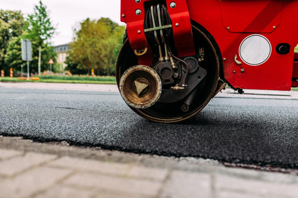 Red road roller paving a new and fresh road. 