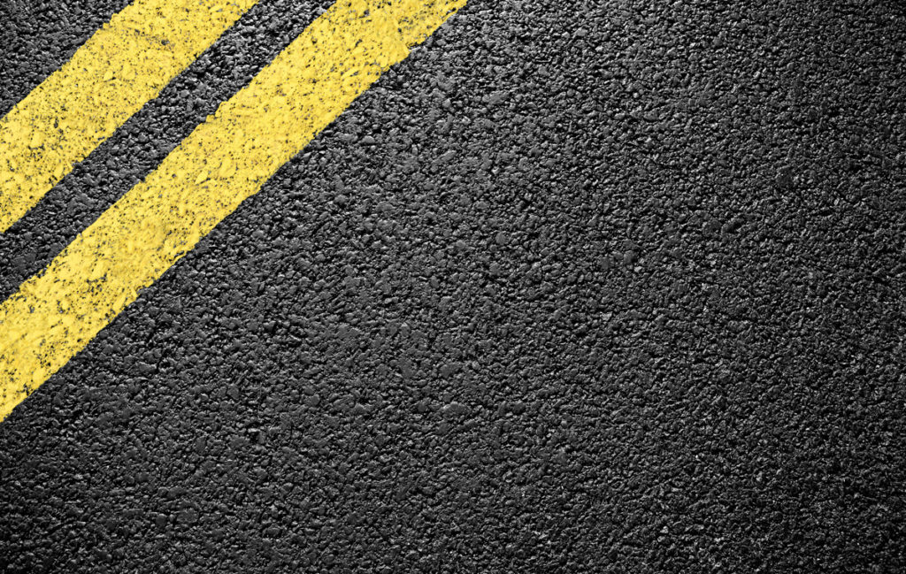 A close-up image of a freshly paved road with yellow road lines in Carlsbad.